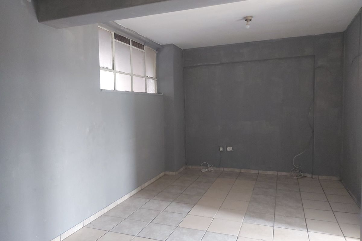 An empty, unfinished living area featuring tiled flooring, an exposed concrete beam, and a multi-pane window, ready for renovation and personalization.