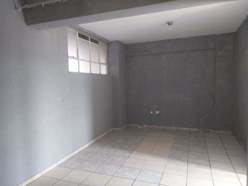 An empty, unfinished living area featuring tiled flooring, an exposed concrete beam, and a multi-pane window, ready for renovation and personalization.