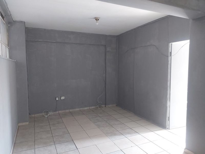 An empty, unfinished living area featuring ceramic floor tiles and exposed electrical wiring, presenting a blank canvas for renovation and interior design.
