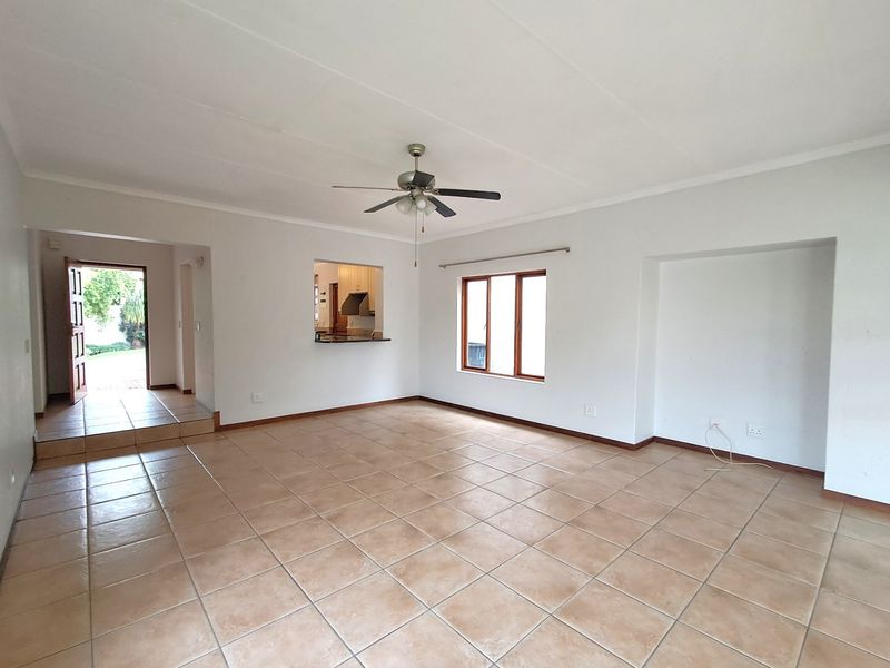 Spacious, light-filled living area featuring neutral tiled flooring, a ceiling fan, and a convenient pass-through window connecting to the kitchen.