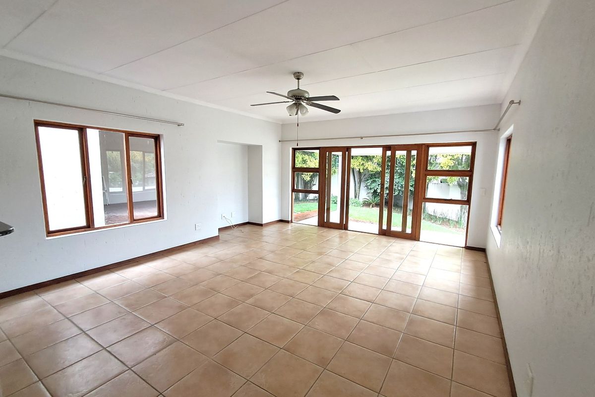 Spacious, empty living area featuring neutral tiled flooring, a ceiling fan, and large wooden sliding doors providing direct access to the garden.
