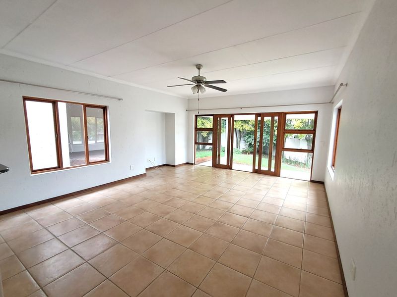 Spacious, empty living area featuring neutral tiled flooring, a ceiling fan, and large wooden sliding doors providing direct access to the garden.