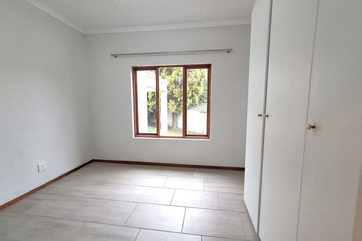 A clean, empty bedroom featuring neutral tiled flooring, built-in cupboards, and wooden window frames, offering a blank canvas for personalization.