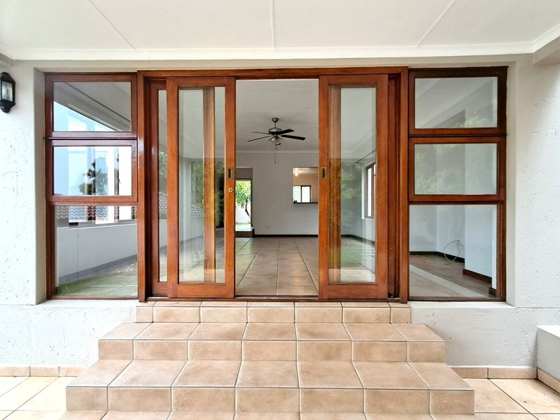 A covered patio area featuring tiled steps and large wooden sliding doors leading into an open-plan interior space with a ceiling fan.