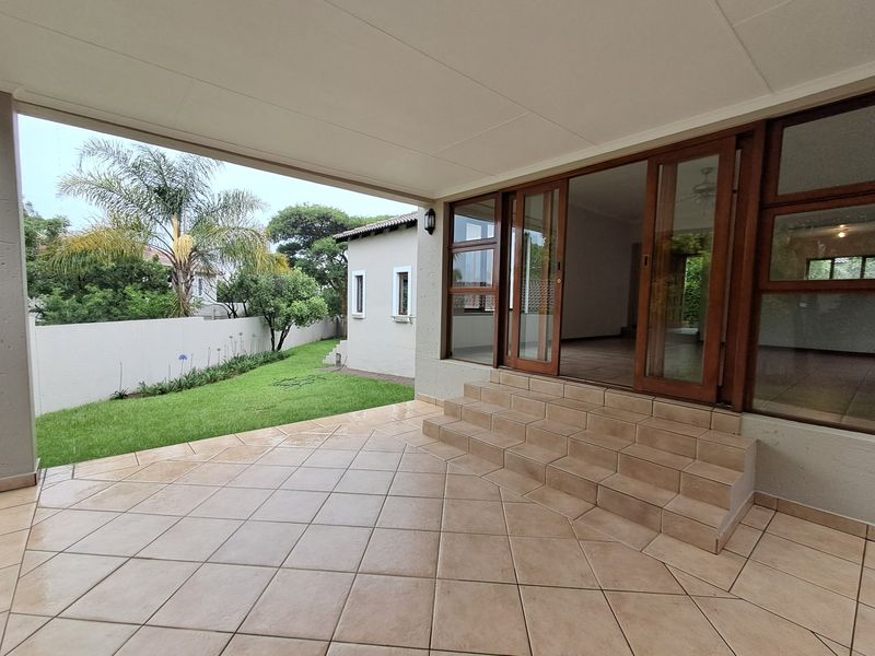 A covered patio area featuring tiled flooring and steps, providing seamless access to the garden through large sliding glass doors.