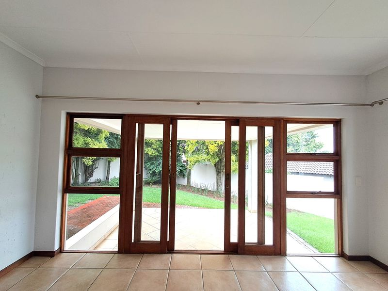 Bright living area featuring large timber sliding doors that open onto a paved patio and garden, finished with neutral ceramic floor tiles.