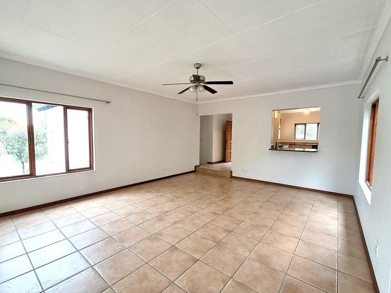 Spacious, empty living area featuring neutral tiled flooring, a ceiling fan, and a convenient serving hatch connecting to the kitchen.