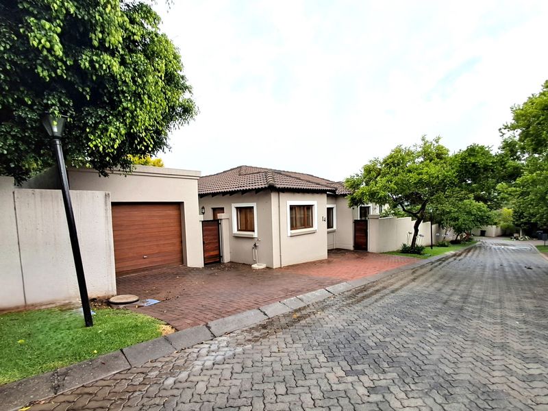 Front elevation of a well-maintained house featuring a paved driveway, integrated garage with wooden door, and secure boundary walls in a quiet street setting.