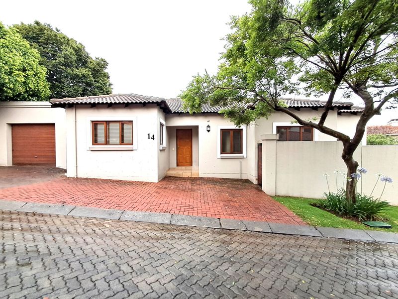Front elevation of a single-story house featuring a brick-paved driveway, single garage, and established garden area.