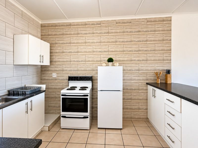 A functional kitchen featuring tiled splashbacks, ample built-in cabinetry, dark countertops, and a freestanding stove, offering a clean and practical workspace.