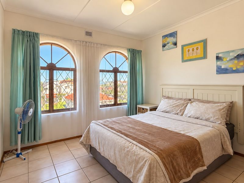 A bright bedroom featuring distinctive arched leaded glass windows, neutral tiled flooring, and a clean, well-maintained interior space.