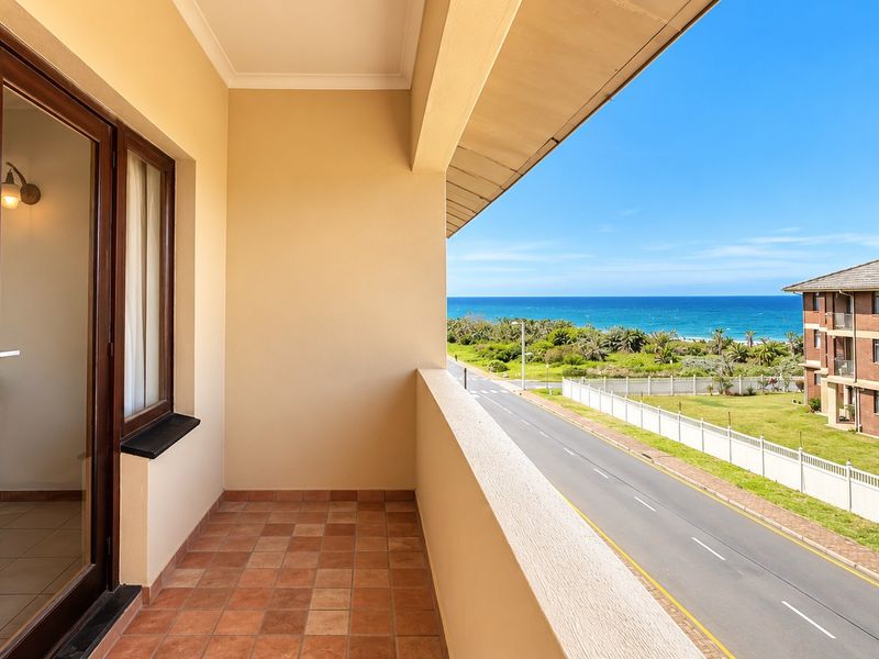A covered balcony featuring terracotta tiling and a sliding glass door, offering scenic views of the nearby road, coastal landscape, and ocean.