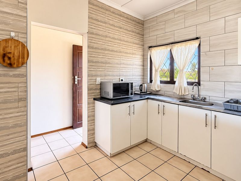 A functional kitchen featuring white cabinetry, tiled walls, and tiled flooring, providing a clean and practical workspace.
