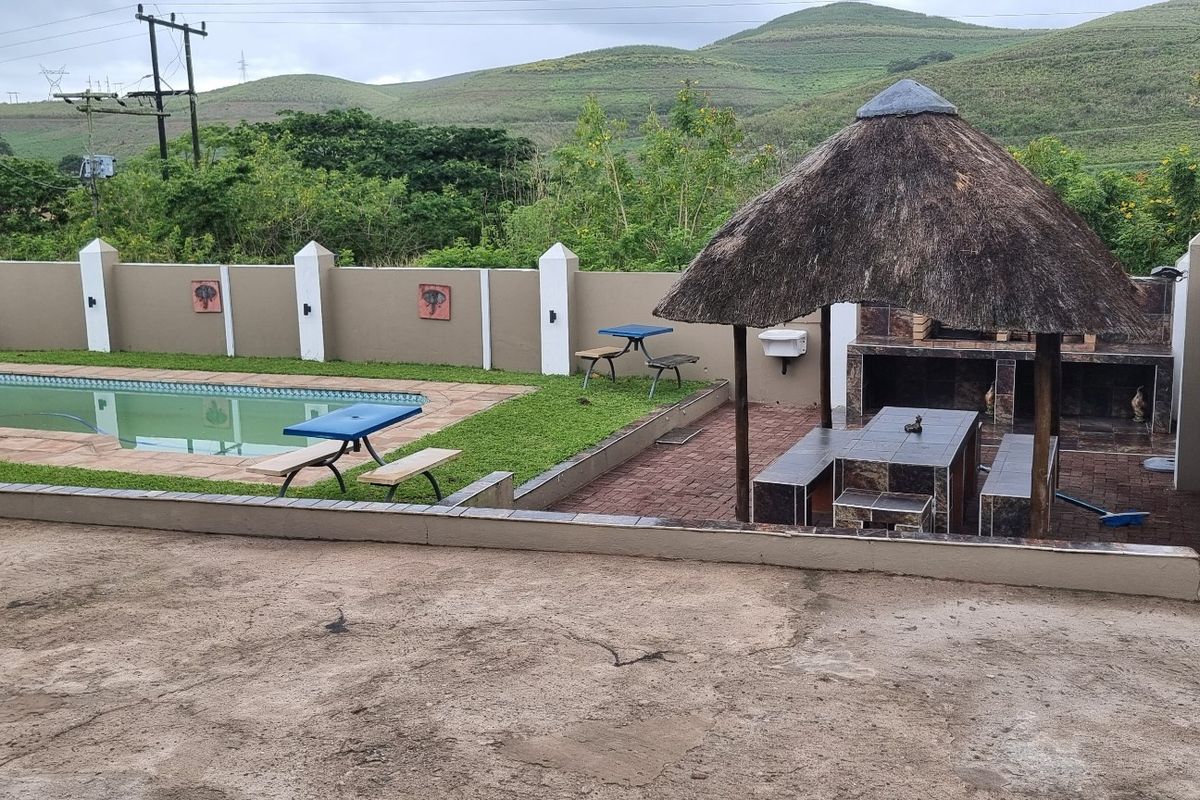 Outdoor entertainment area featuring a swimming pool, a thatched lapa with a built-in braai, and a perimeter wall with scenic mountain views.