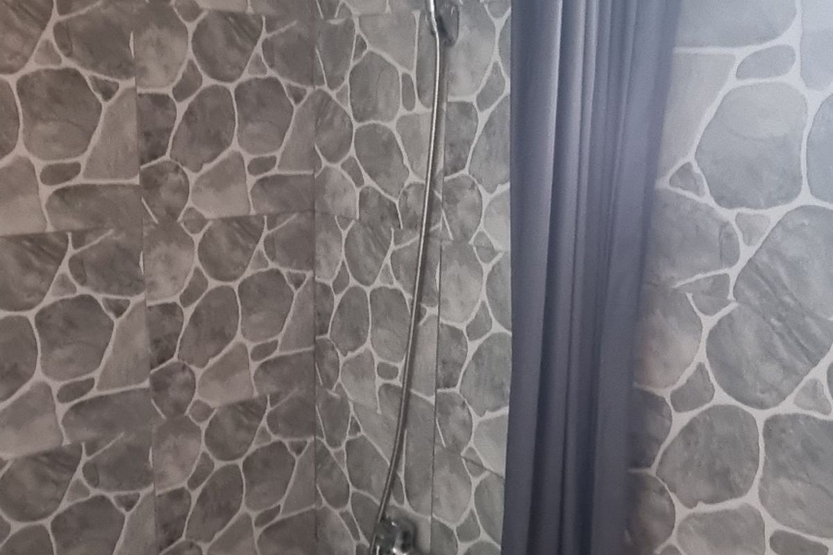 A compact bathroom featuring stone-effect wall and floor tiling, a pedestal basin, and a shower area with a curtain rail.
