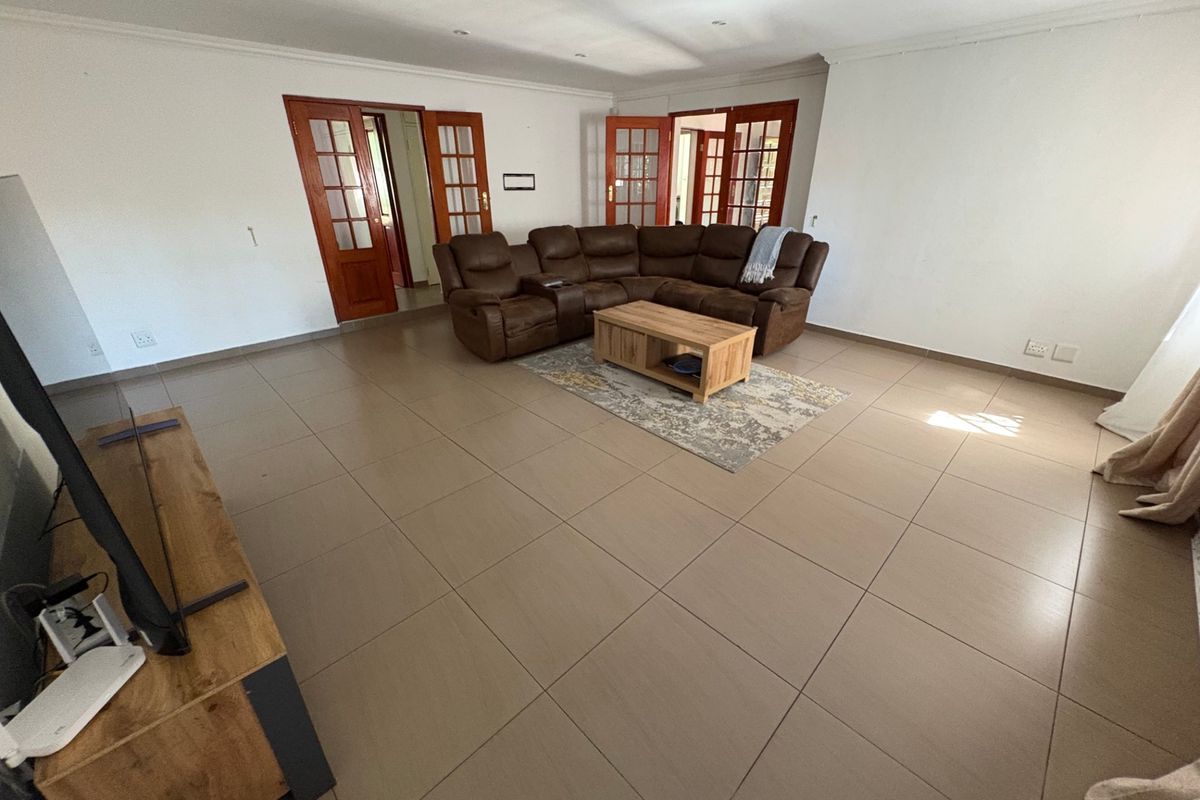 Spacious living room featuring large format floor tiles, recessed lighting, and multiple sets of wooden framed glass doors providing access to adjacent areas.