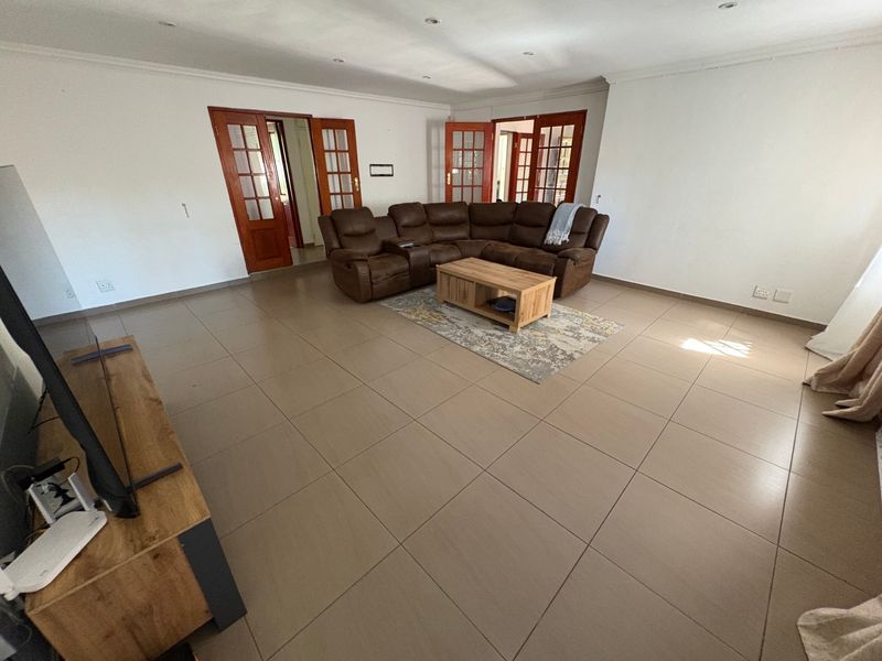 Spacious living room featuring large format floor tiles, recessed lighting, and multiple sets of wooden framed glass doors providing access to adjacent areas.