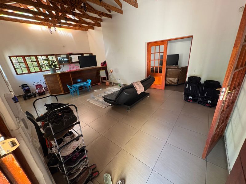 Spacious living area featuring exposed timber rafters, large tiled flooring, and a built-in wooden bar counter, offering a versatile open-plan layout.