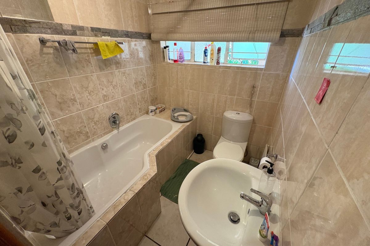 A compact bathroom featuring fully tiled walls and floors, a built-in bathtub, a pedestal washbasin, and a standard toilet.