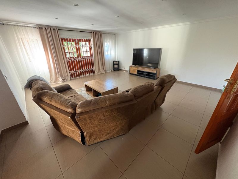 Spacious living room featuring neutral tiled flooring, recessed lighting, and a sliding door with a security gate providing access to the exterior.