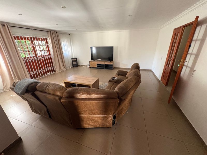 Spacious living room featuring large format floor tiles, recessed lighting, and direct access to the exterior through a secure timber door.