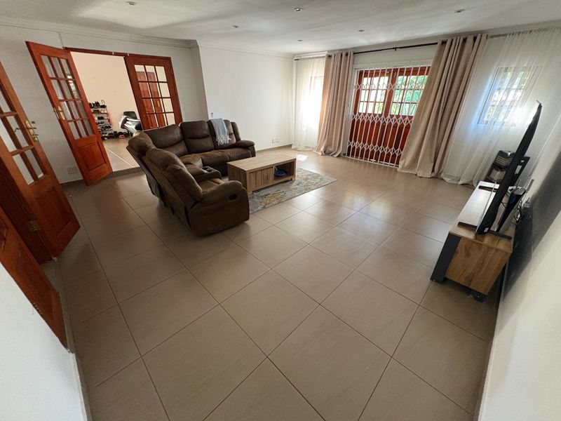 Spacious living room featuring large format floor tiles, recessed lighting, and wooden french doors leading to an adjacent room and outdoor area.