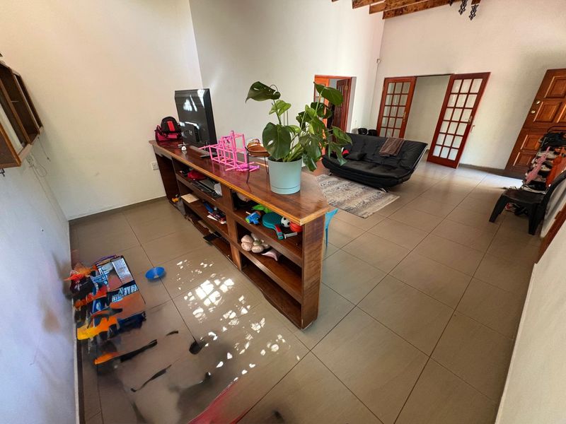 Spacious living area featuring exposed timber ceiling beams, tiled flooring, and a built-in wooden partition shelf, offering a versatile layout with access to adjacent rooms.
