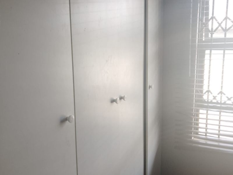 A bedroom featuring built-in cupboards, security bars on the window, and venetian blinds, offering a functional storage space.