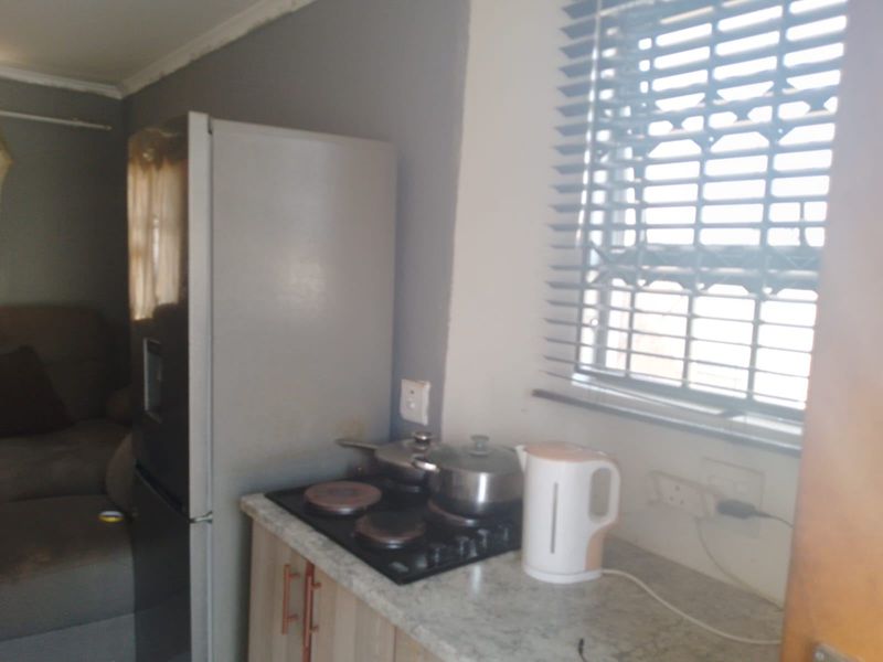 A compact kitchen area featuring a built-in hob, laminate countertops, and cabinetry, illuminated by natural light through a window with venetian blinds.