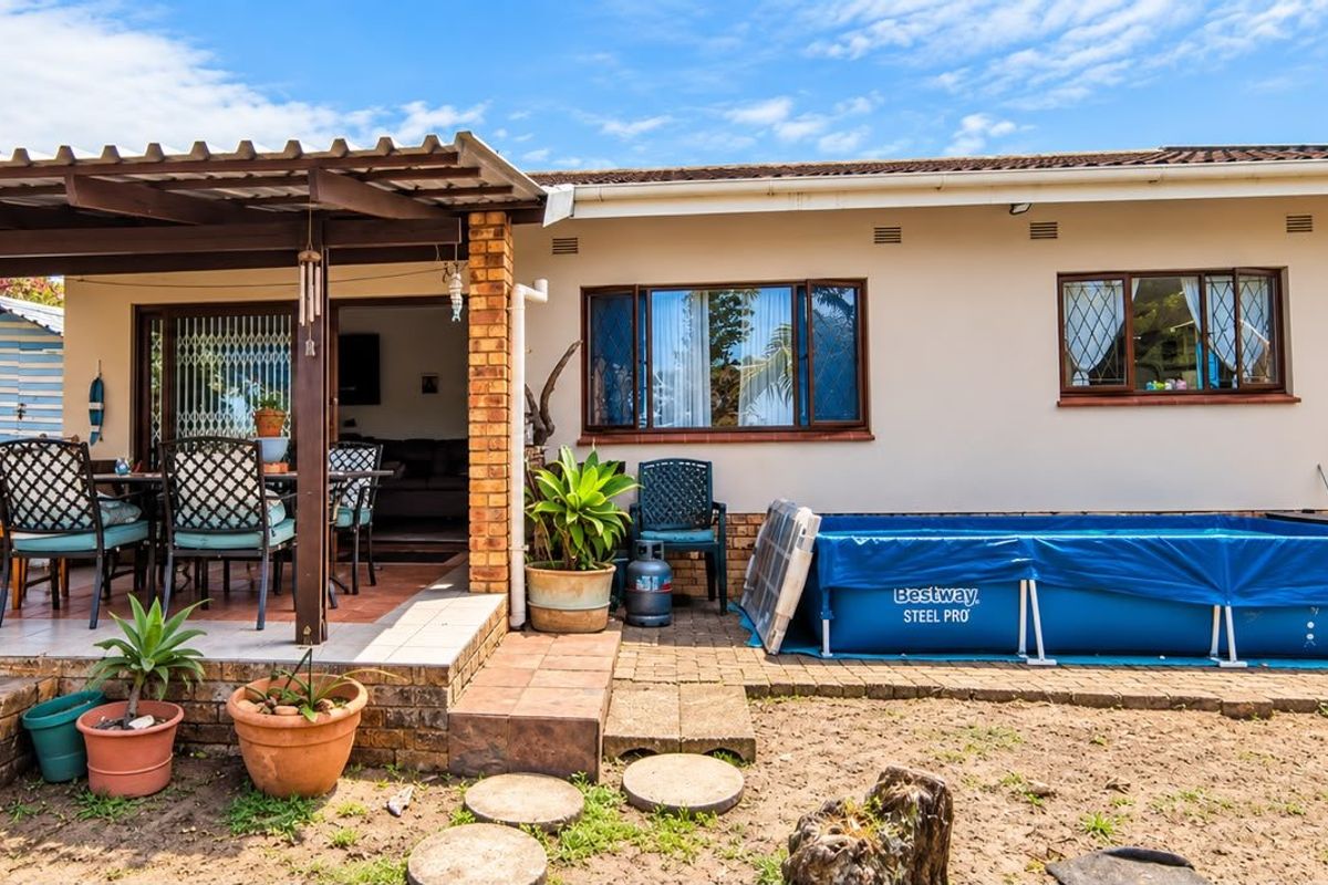 Rear view of the house featuring a covered patio with brick pillars, tiled flooring, and access to the interior via a sliding glass door.