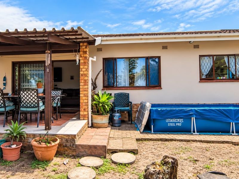 Rear view of the house featuring a covered patio with brick pillars, tiled flooring, and access to the interior via a sliding glass door.