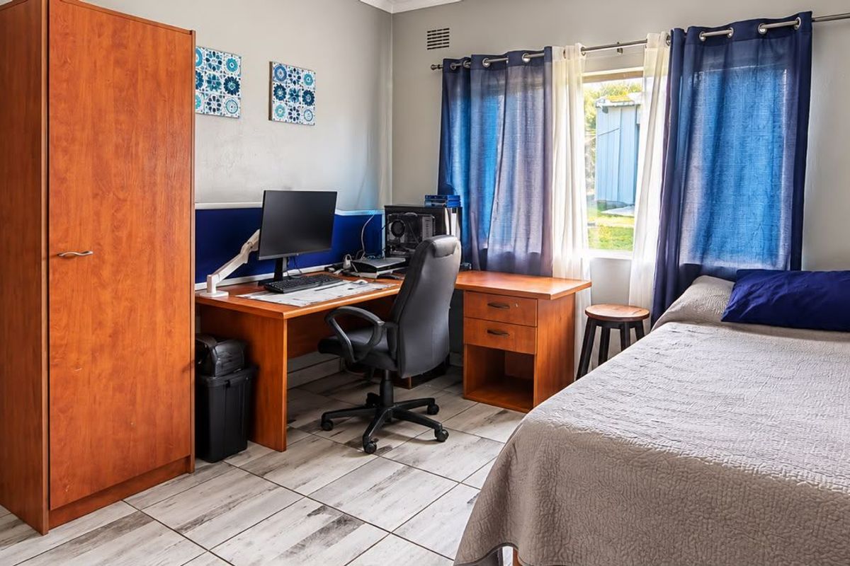 A functional bedroom featuring tiled flooring and a window, currently utilized as a combined sleeping and workspace area.