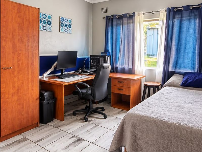 A functional bedroom featuring tiled flooring and a window, currently utilized as a combined sleeping and workspace area.