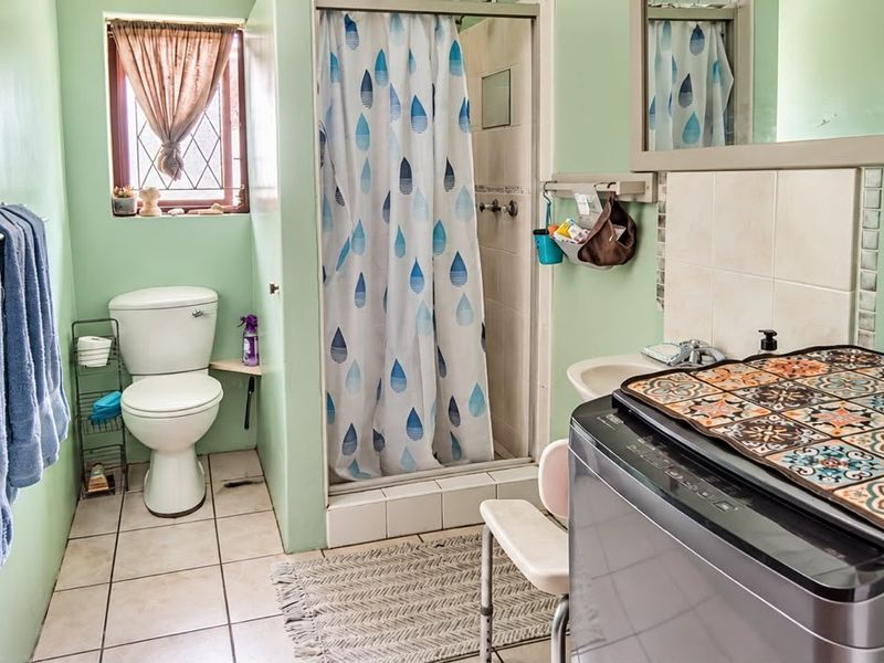 A functional bathroom featuring a shower enclosure, toilet, and washbasin with tiled flooring and light green wall finishes.