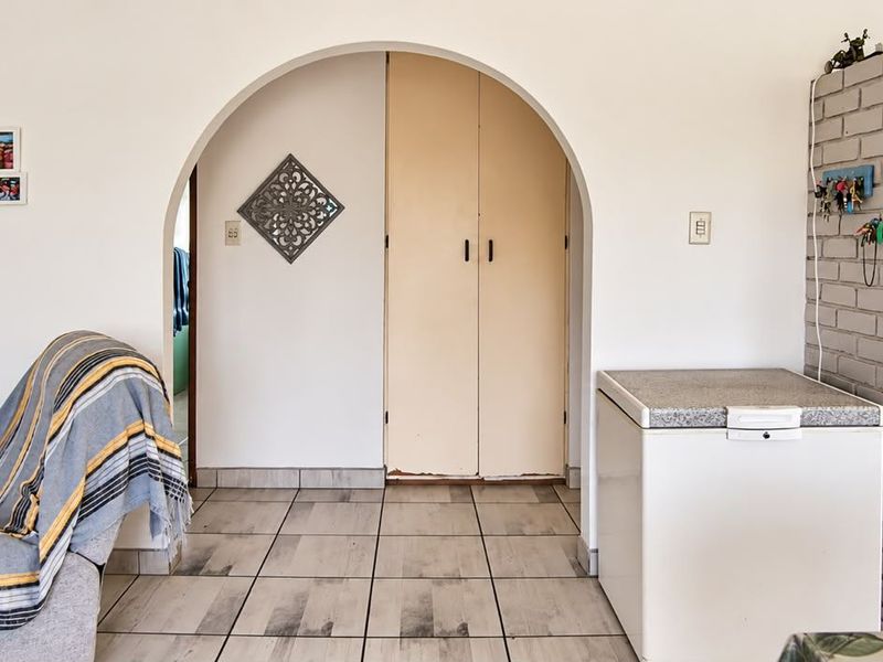 Living area featuring tiled flooring, an arched doorway leading to a built-in cupboard, and an exposed brick pillar detail.