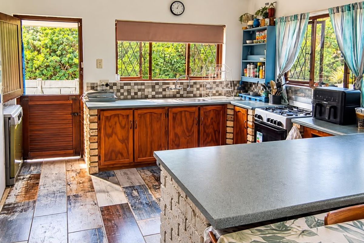 A rustic kitchen featuring wooden cabinetry with brick bases, laminate countertops, a double sink, and a freestanding stove, with direct access to the exterior.