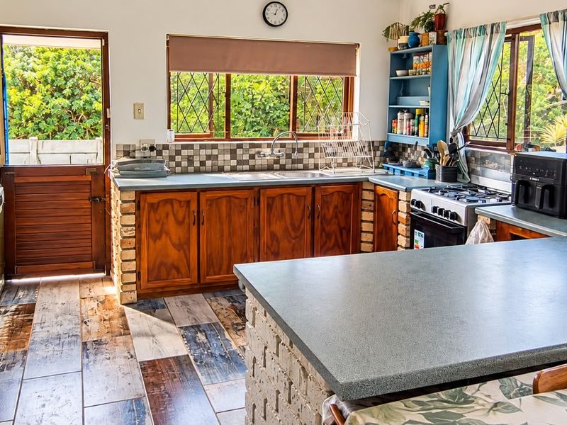 A rustic kitchen featuring wooden cabinetry with brick bases, laminate countertops, a double sink, and a freestanding stove, with direct access to the exterior.