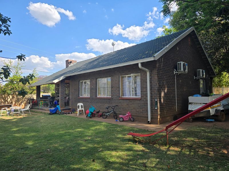 Rear view of a brick house featuring a tiled roof, security bars on windows, and a covered patio area overlooking the garden.