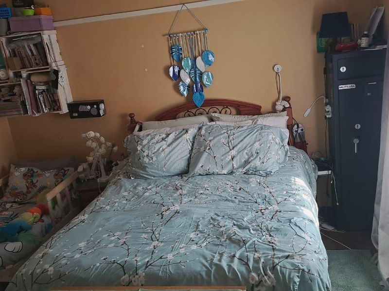 A bedroom featuring a standard layout with wall-mounted shelving and window treatments, currently showing signs of wear on the wall surfaces.