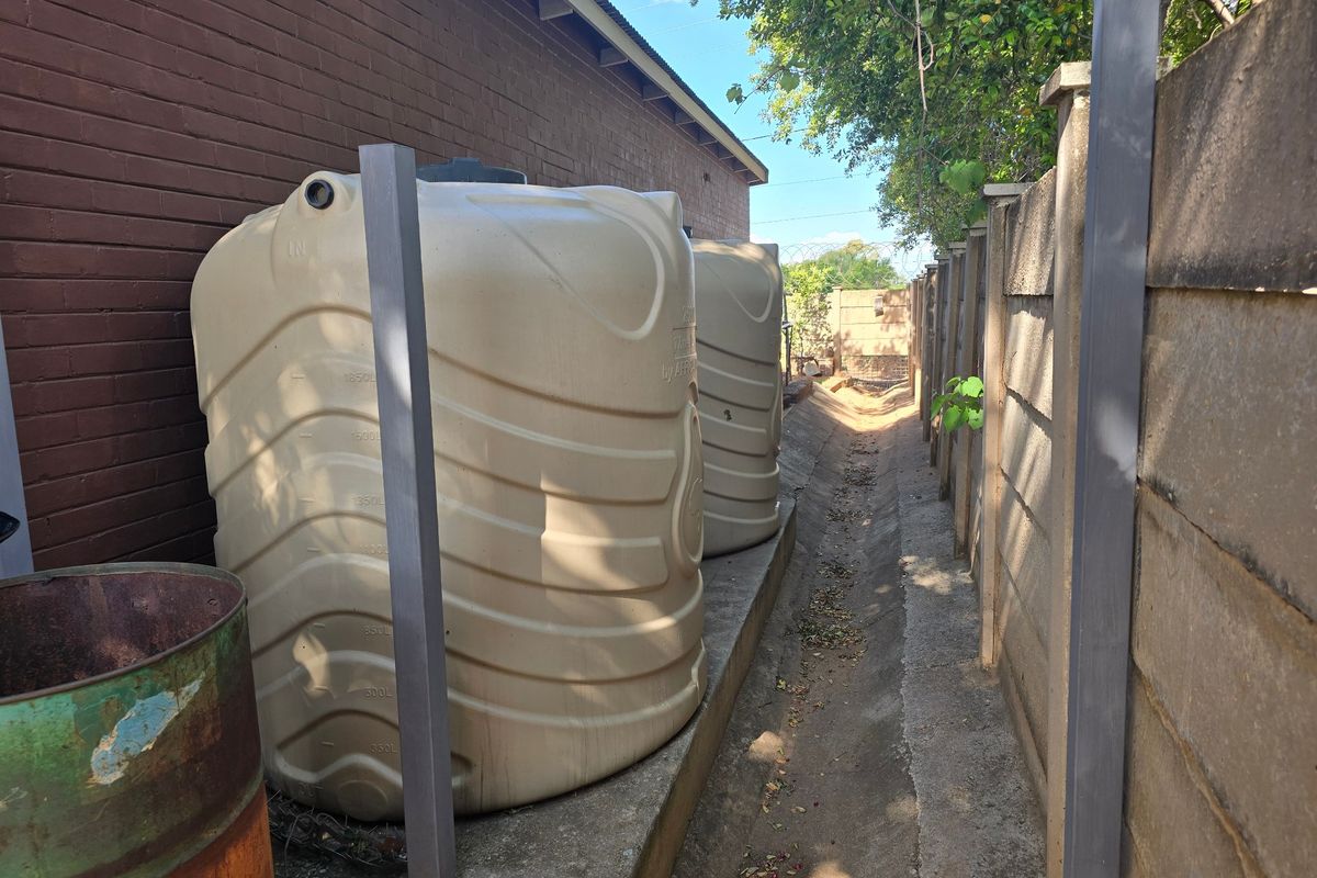 Side exterior area featuring two large water storage tanks positioned along a brick wall and a concrete drainage channel.