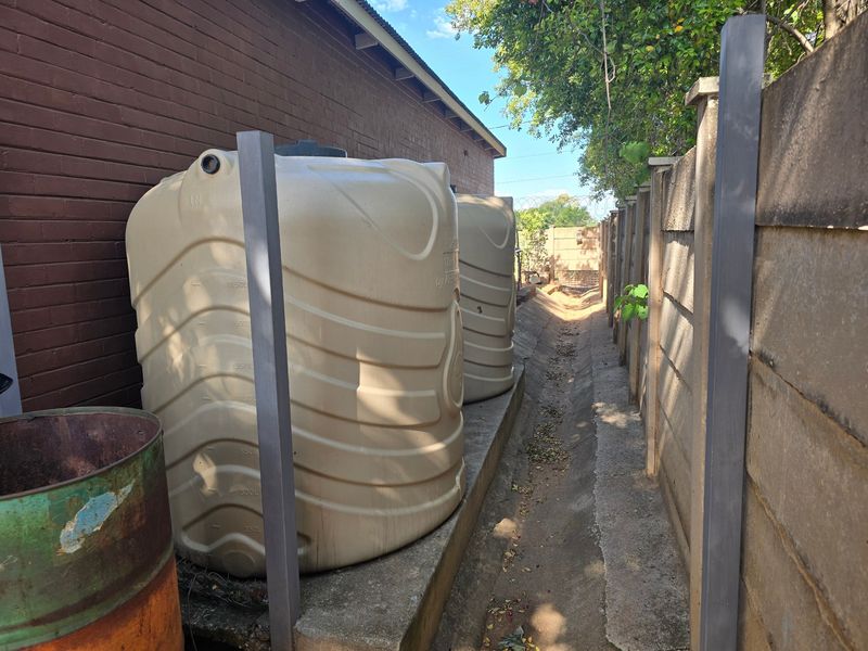 Side exterior area featuring two large water storage tanks positioned along a brick wall and a concrete drainage channel.