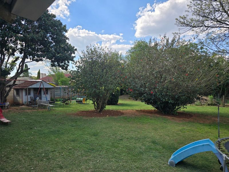 A spacious backyard featuring a well-maintained lawn, mature trees, and a garden shed, providing a private outdoor area for recreation.