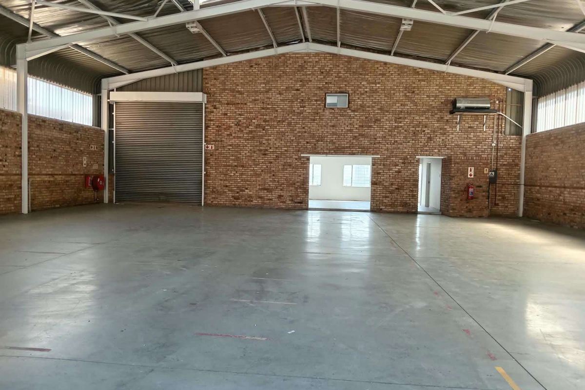 Spacious industrial warehouse unit featuring high ceilings with exposed steel trusses, durable concrete flooring, and a large roller shutter door for easy access.