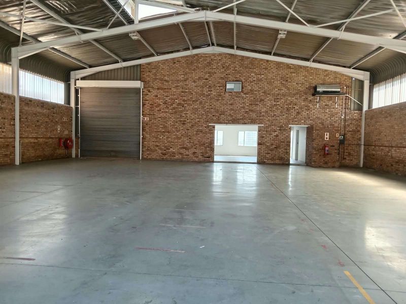 Spacious industrial warehouse unit featuring high ceilings with exposed steel trusses, durable concrete flooring, and a large roller shutter door for easy access.