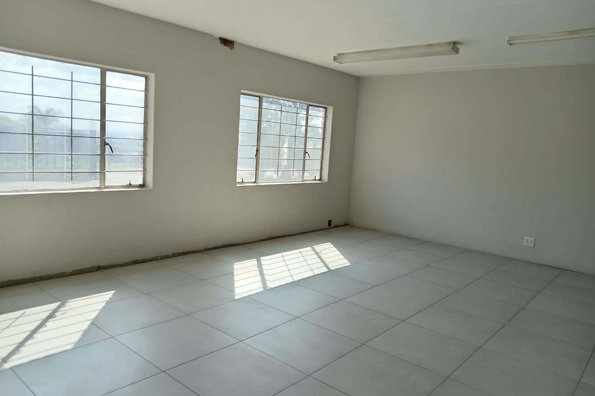 An empty, open-plan office space featuring tiled flooring, large windows with security bars, and fluorescent lighting, ready for customization.