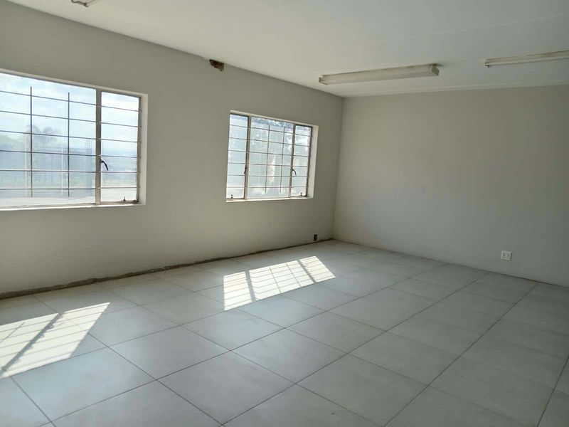 An empty, open-plan office space featuring tiled flooring, large windows with security bars, and fluorescent lighting, ready for customization.
