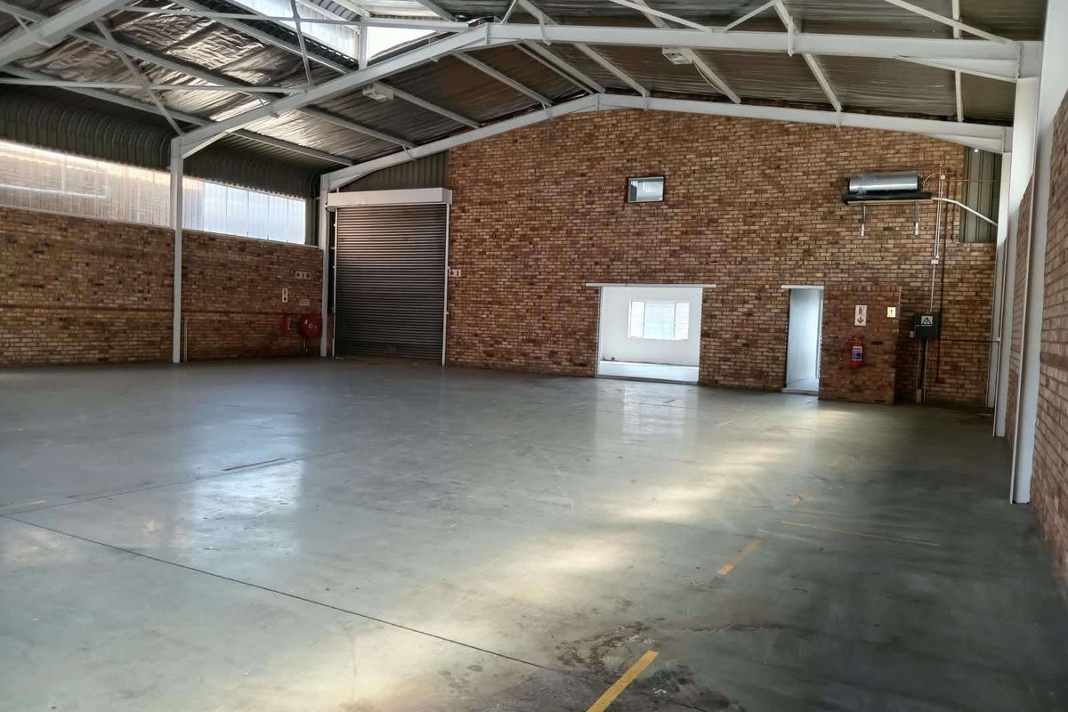 Spacious industrial warehouse unit featuring high exposed steel truss ceilings, durable concrete flooring, and large roller shutter access.
