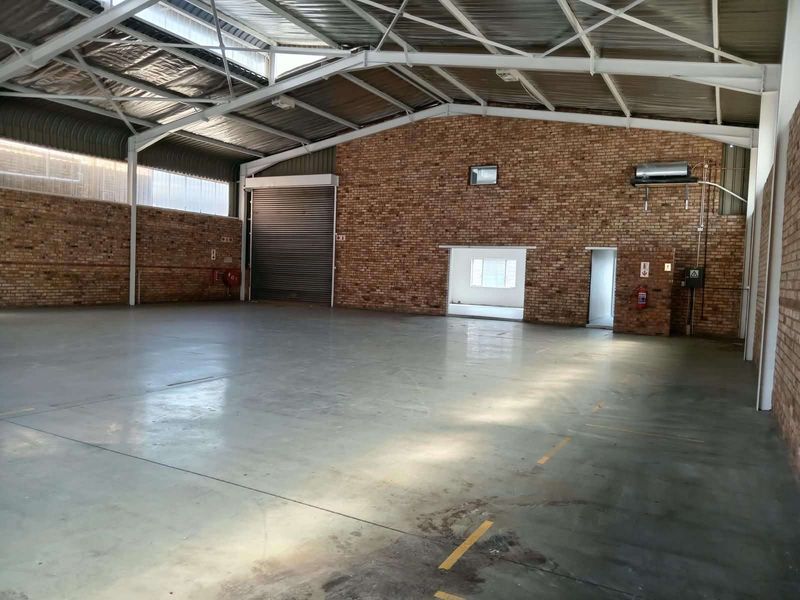 Spacious industrial warehouse unit featuring high exposed steel truss ceilings, durable concrete flooring, and large roller shutter access.