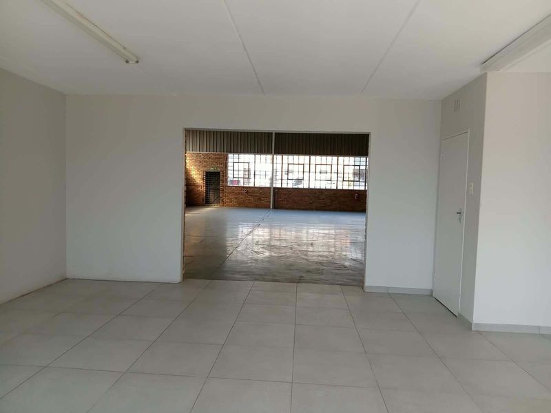 Spacious open-plan industrial unit featuring tiled flooring in the front area, transitioning to a large warehouse space with exposed brick and industrial windows.