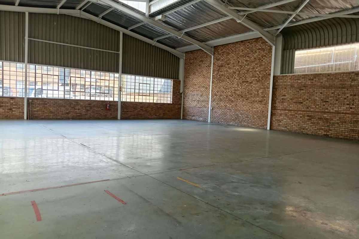 Spacious industrial warehouse unit featuring exposed brick walls, high steel-truss ceilings, polished concrete flooring, and large steel-framed windows providing ample natural light.